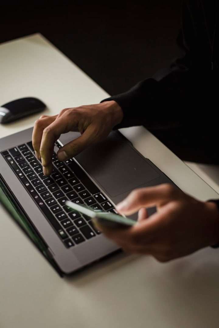 High angle crop male in black clothes browsing contemporary netbook and mobile phone while working in office